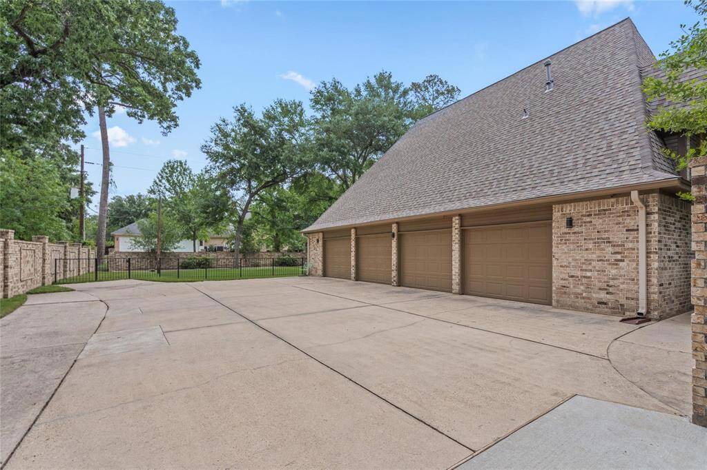 Expansive driveway leads to a four-car brick garage, nestled among mature trees with a fenced yard for privacy and ample parking.
