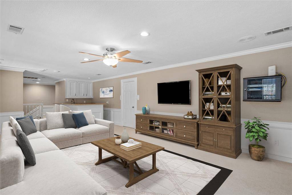 This spacious living room features a cozy sectional sofa, ceiling fan, and built-in entertainment unit. It's complemented by a large wooden cabinet and modern decor. The area is bright and airy, with an open connection to adjacent spaces.