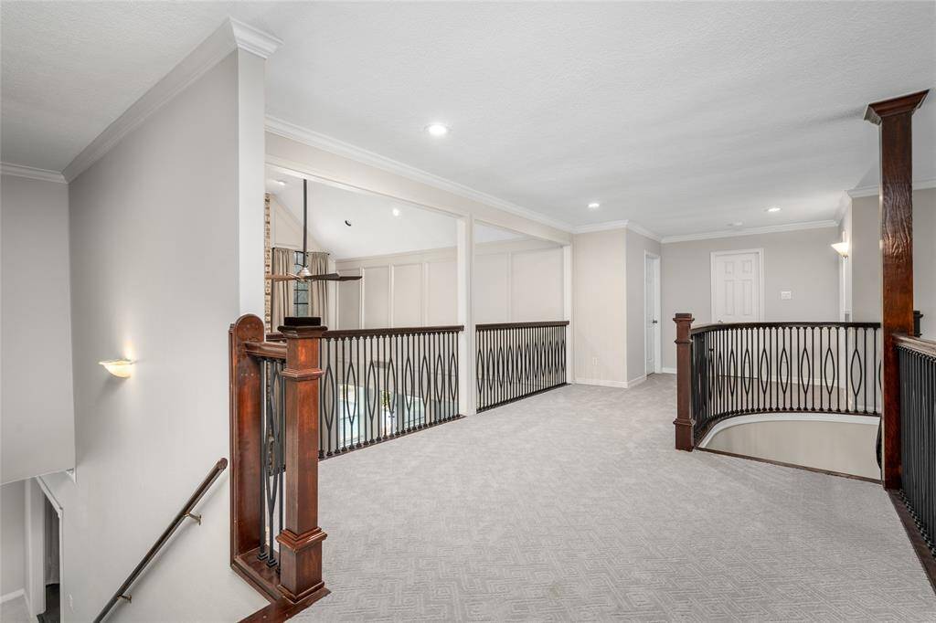Bright and spacious upper landing with elegant wrought iron railings and plush carpeting, featuring recessed lighting and neutral walls for a modern, airy feel.