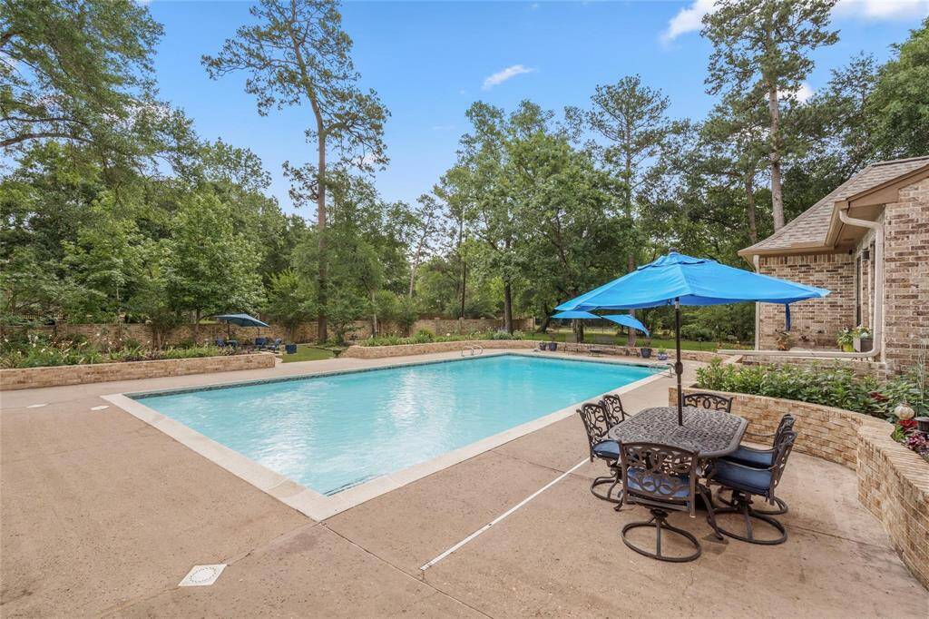 This photo showcases a beautiful backyard with a large, inviting swimming pool surrounded by lush greenery. The area features a spacious patio with stylish outdoor furniture and blue umbrellas, perfect for relaxation and entertaining.
