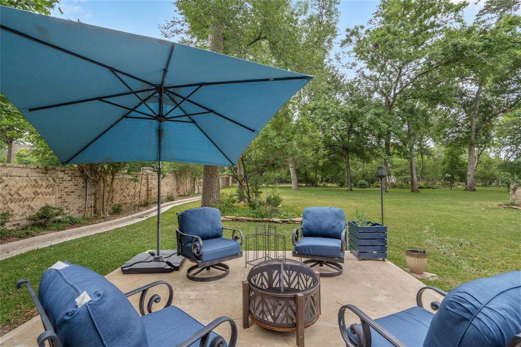 Discover a tranquil backyard oasis featuring plush blue seating, a large umbrella, and a cozy fire pit, all surrounded by lush greenery and mature trees—ideal for relaxation and entertaining.