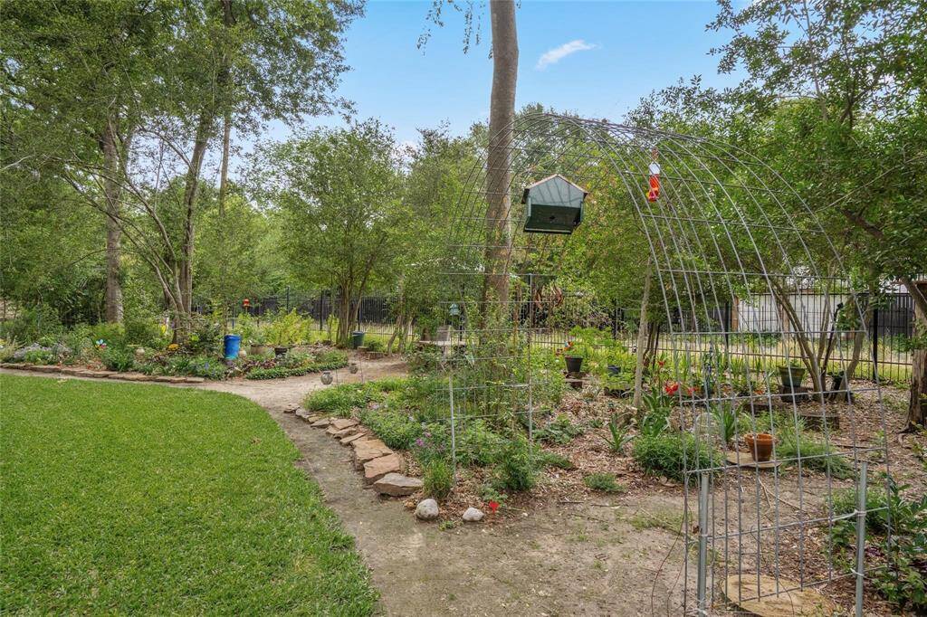 Charming garden space with a lush lawn, mature trees, and a quaint pathway. Features a decorative metal arbor, birdhouse, and various plants, creating a serene outdoor retreat.