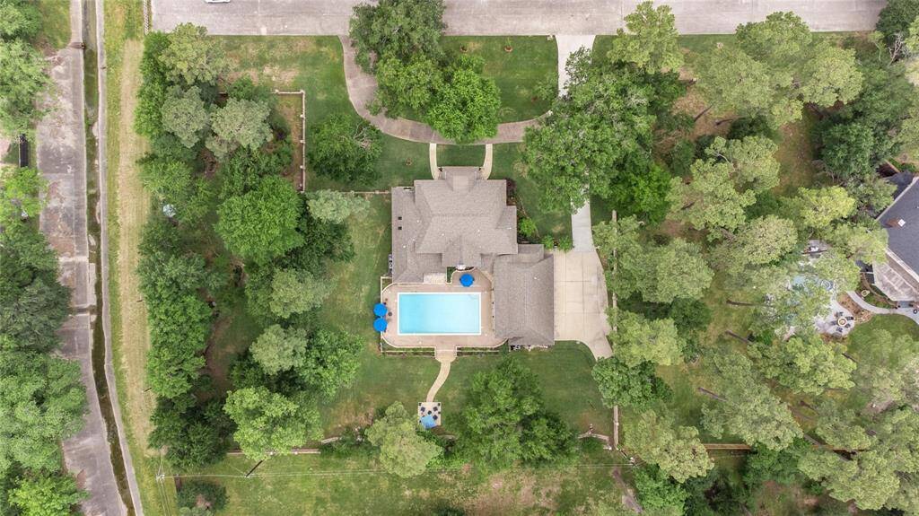 This aerial view showcases a spacious home with a large backyard, featuring a swimming pool and surrounded by lush greenery. The property offers ample privacy and a driveway leading to the house. Perfect for those seeking a serene, nature-filled setting.