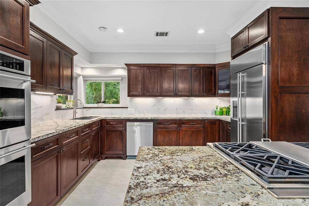 This spacious kitchen features rich wooden cabinetry, granite countertops, stainless steel appliances, and a large window for natural light, providing a modern and elegant cooking space.