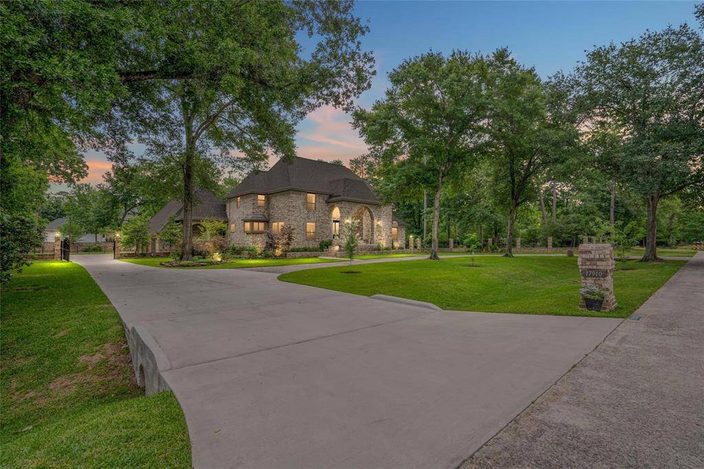 Discover this elegant stone home with a steep roof, beautifully nestled among mature trees. A wide, curved driveway welcomes you, surrounded by lush lawns and pristine landscaping, offering a serene and inviting atmosphere.