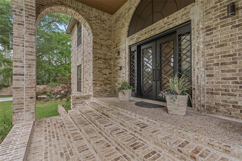 This elegant home entrance features a grand brick archway and steps leading to double doors with decorative glass. Flanked by potted plants, it offers a welcoming and stylish first impression.