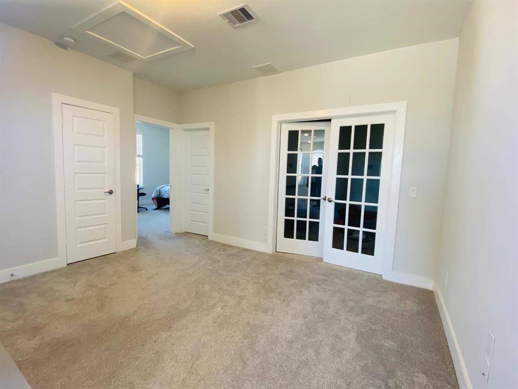This room features soft carpeting, neutral walls, and three doors, including elegant glass French doors that enhance natural light. Ideal for a home office or study.