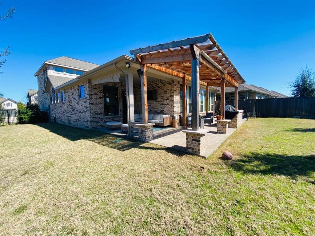 This photo showcases a spacious backyard with a well-maintained lawn and a covered patio featuring a pergola. The brick exterior of the house adds charm, and the outdoor living area is perfect for relaxing or entertaining.
