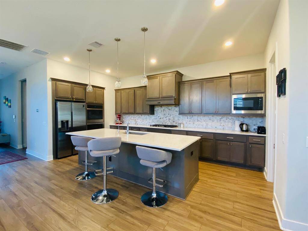 This kitchen features modern stainless steel appliances, ample dark wood cabinetry, and a stylish island with seating, complemented by elegant pendant lighting and a sleek backsplash.