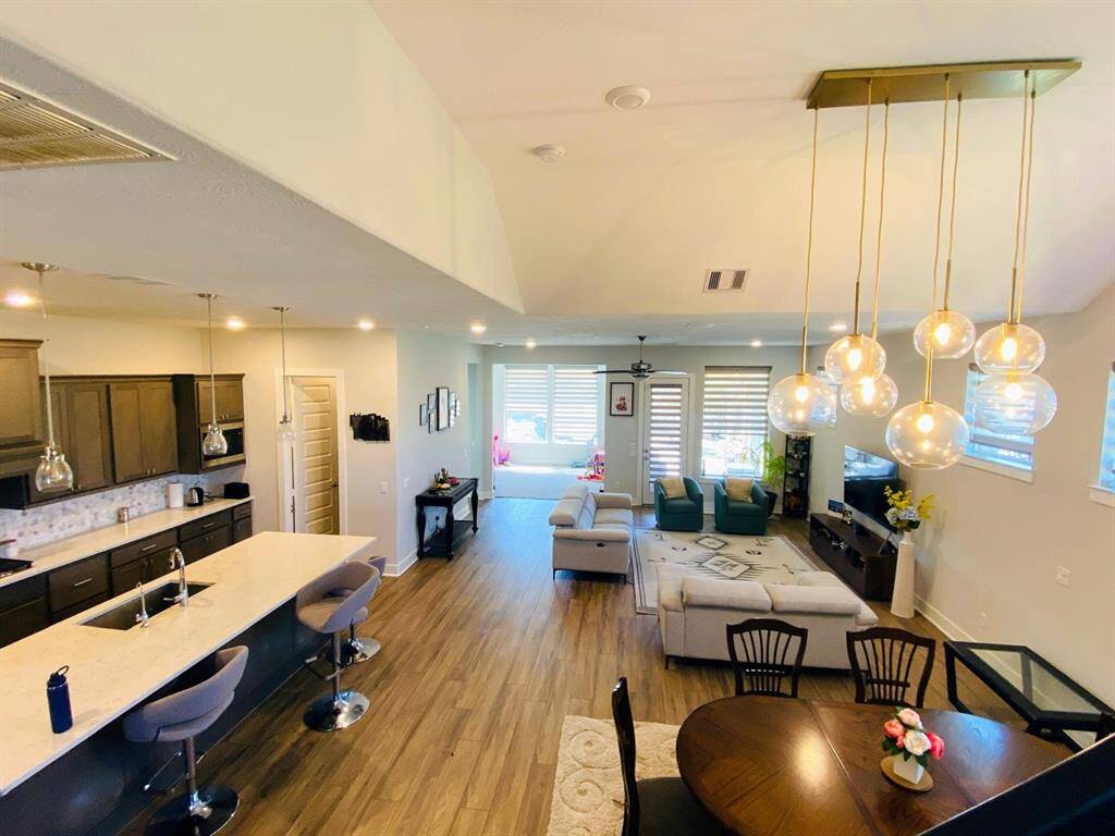 This open-concept living area features a modern kitchen with an island, elegant pendant lighting, and wood flooring. The space flows into a cozy living room with large windows and a comfortable seating area, creating a bright and inviting atmosphere.