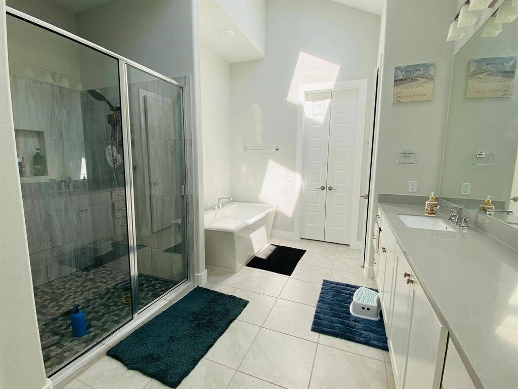 This bathroom features a spacious layout with a large glass-enclosed shower, a separate bathtub, dual sinks with ample counter space, and a modern aesthetic with bright natural lighting.