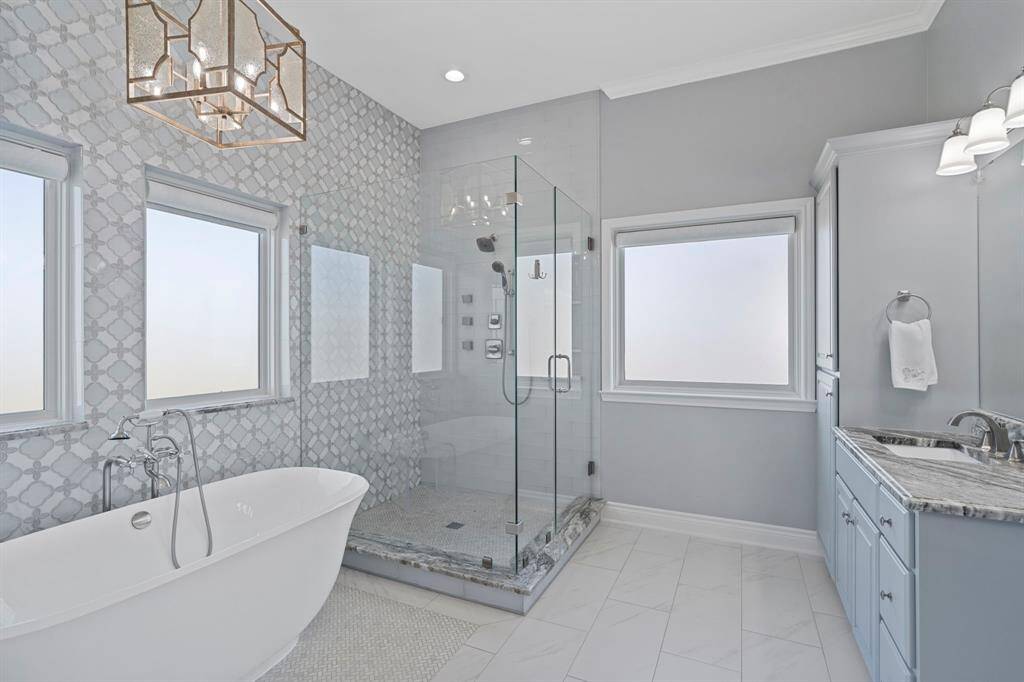 The primary bathroom has tile floors, accent wall, walk-in shower with glass door, and separate soaking tub with chandelier above.