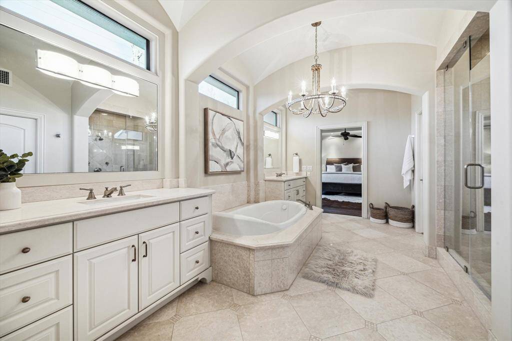 Large spa worthy ensuite bathroom with two vanities, arched ceiling and a chandelier over the tub.