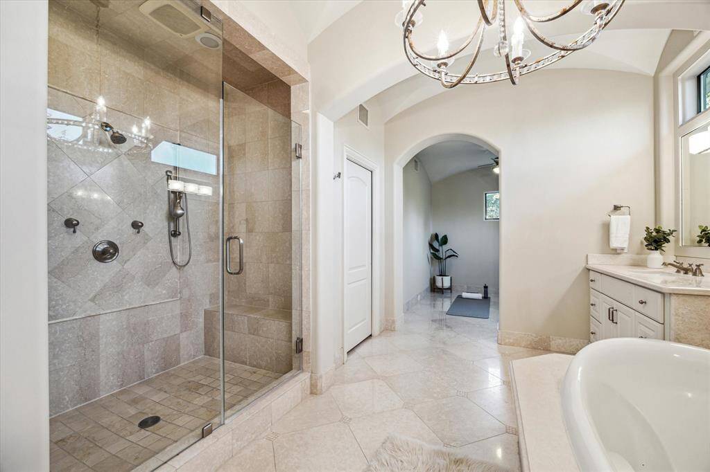 Spacious glass enclosed shower with a shower head as well as a handheld sprayer and bench.