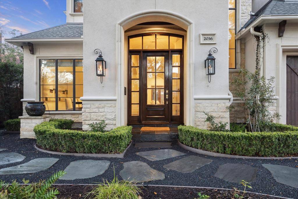 Lush landscaping creates a warm and inviting entrance, guiding guests to the front door, which is elegantly framed by two charming gas lanterns.