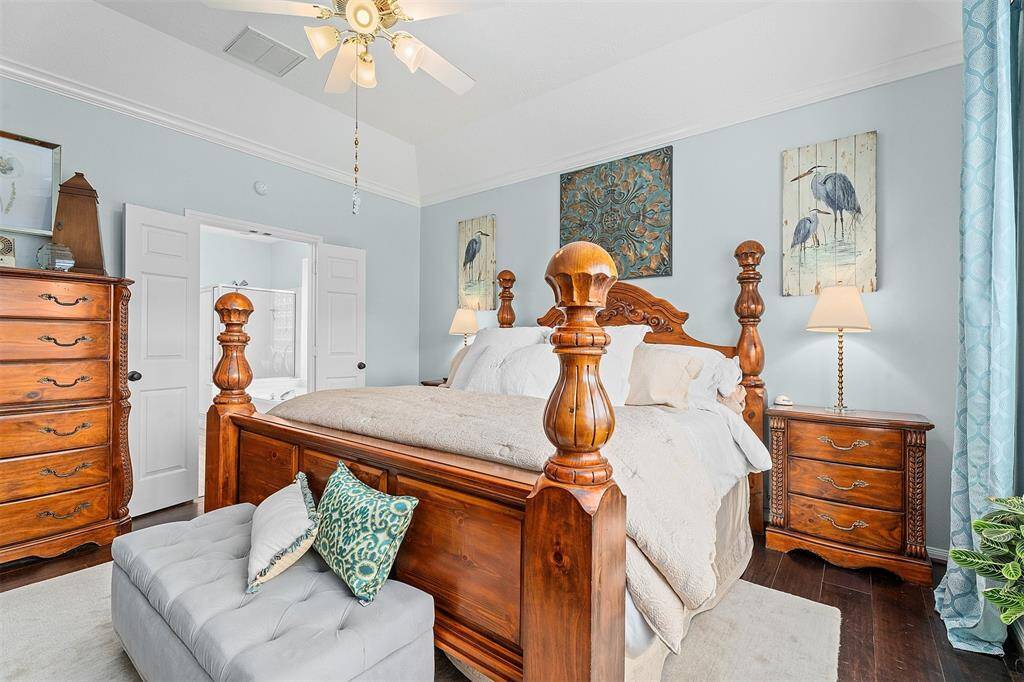 The primary bedroom has a soft blue wall color, large windows with shutters for natural light, and a ceiling fan for comfort. The room is spacious and well-lit, offering a cozy and stylish retreat.