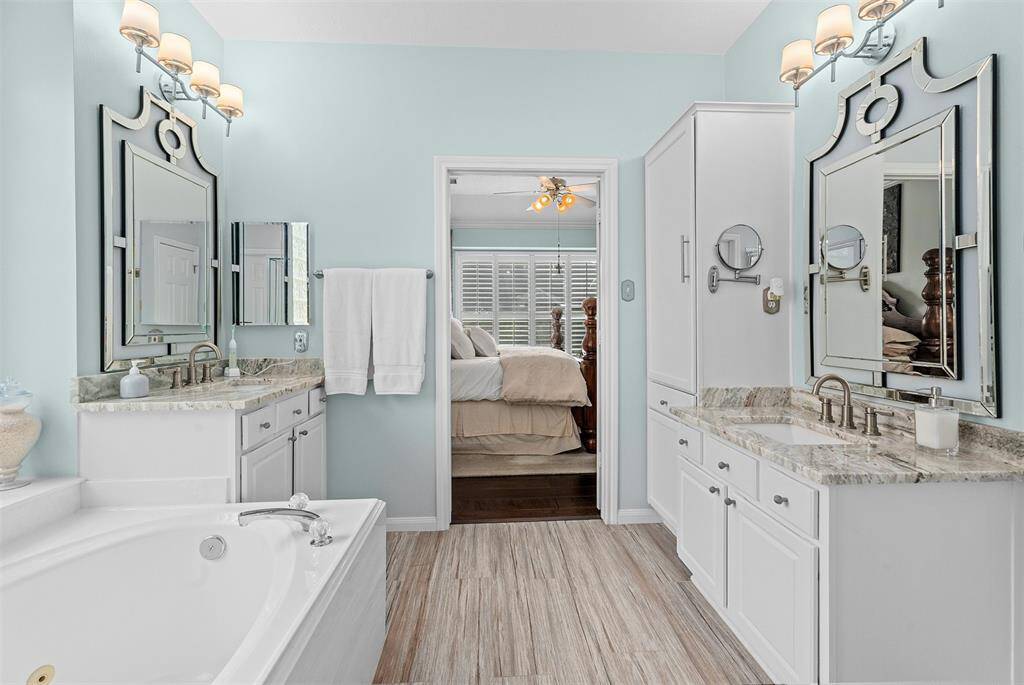 Indulge in the luxurious primary en-suite featuring a whirlpool tub, dual vanities, and double walk in closets.This bathroom features a modern design with an upgraded countertop, elegant faucet, and a large decorative mirror. A unique wall art piece adds character to the neutral-toned walls.