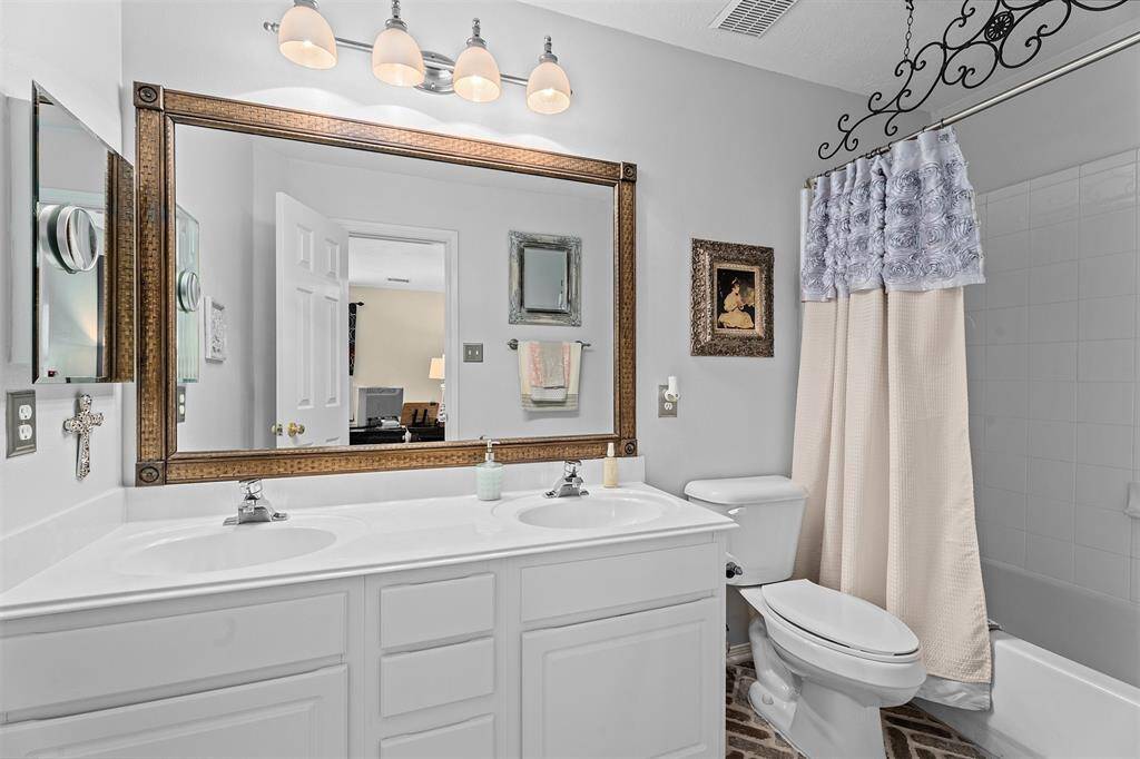 Immaculate secondary bath featuring double sinks for added convenience. This bathroom features a double vanity with a large framed mirror, elegant lighting, and a shower-tub combo. The room is bright and inviting, with  modern fixtures.