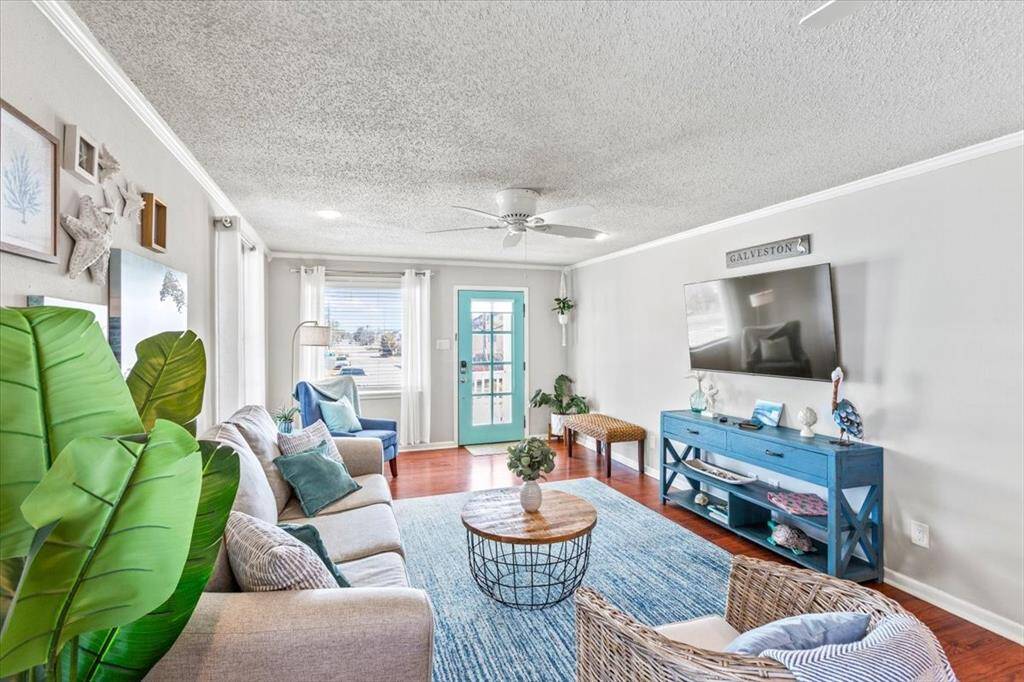 This is a bright and airy living room featuring contemporary decor, hardwood floors, a ceiling fan, and ample natural light from windows and a glass door leading to an outdoor area.