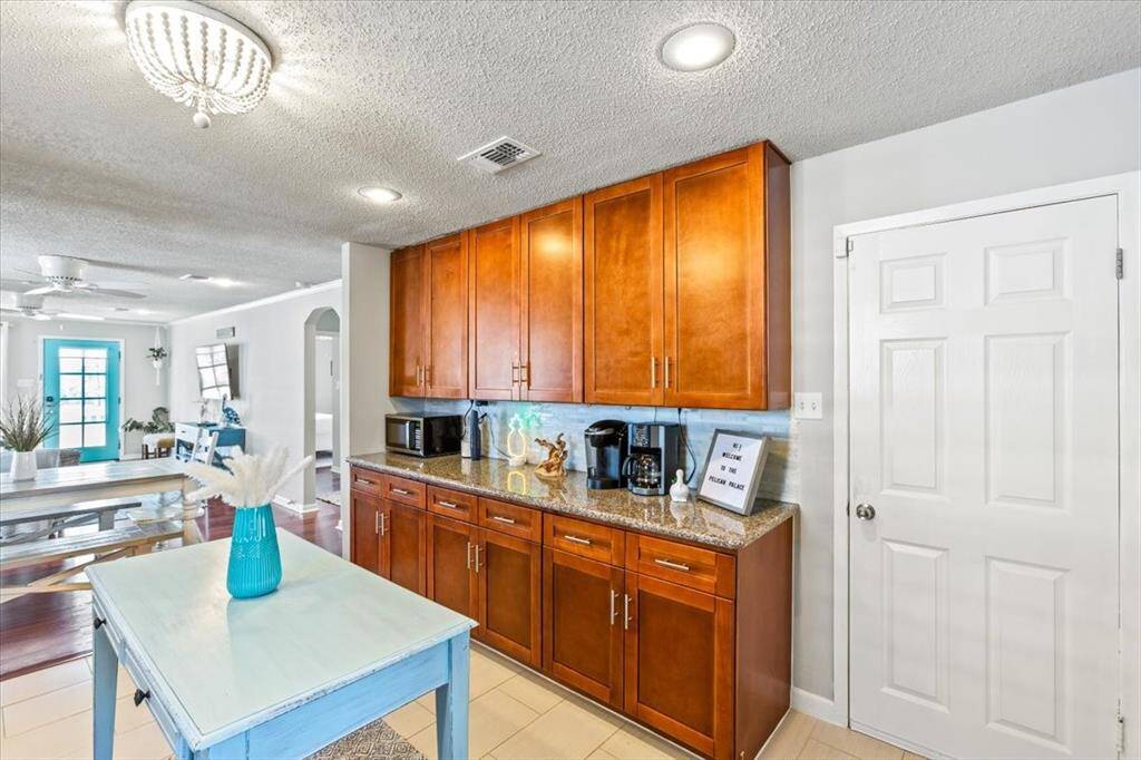 This photo showcases a bright, open-concept kitchen with rich wooden cabinetry, granite countertops, and a modern backsplash. The space flows seamlessly into a dining area, highlighted by a chic light fixture and contemporary decor. A door suggests convenient access, possibly to a pantry or utility room.