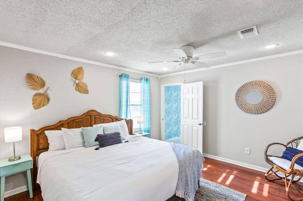 This is a bright and airy bedroom featuring a wooden bed frame, tropical-inspired decor, a ceiling fan, and hardwood floors. It includes a private access door, likely leading to an ensuite or outdoor area.