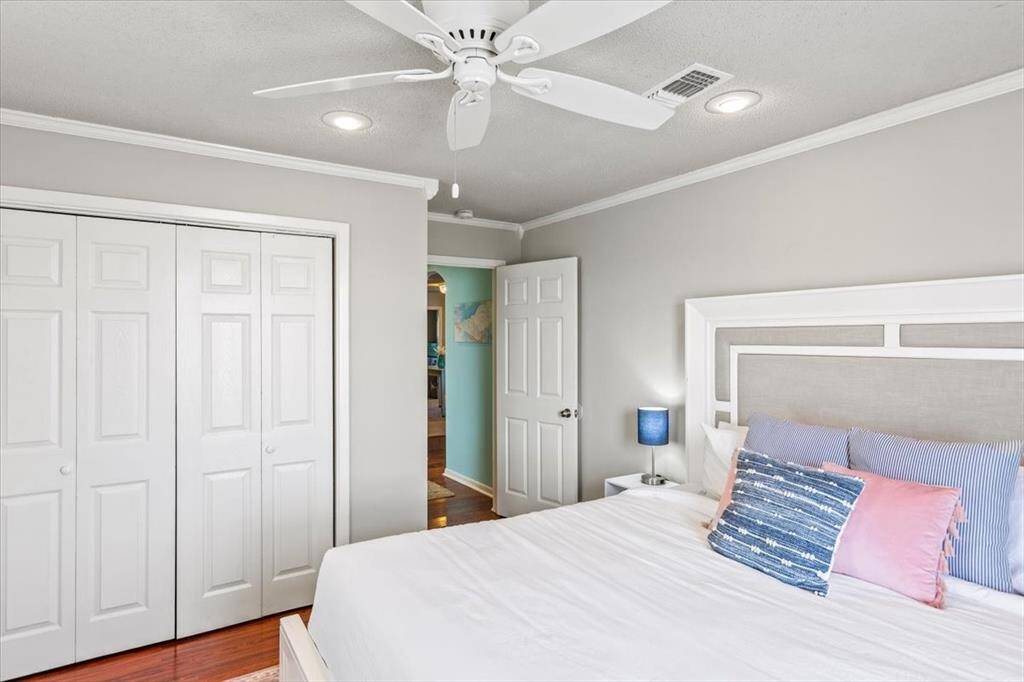 This is a bright, well-maintained bedroom featuring hardwood floors, a ceiling fan, and ample closet space with white double doors. The room is painted in a neutral color scheme and has a doorway leading to another part of the house.