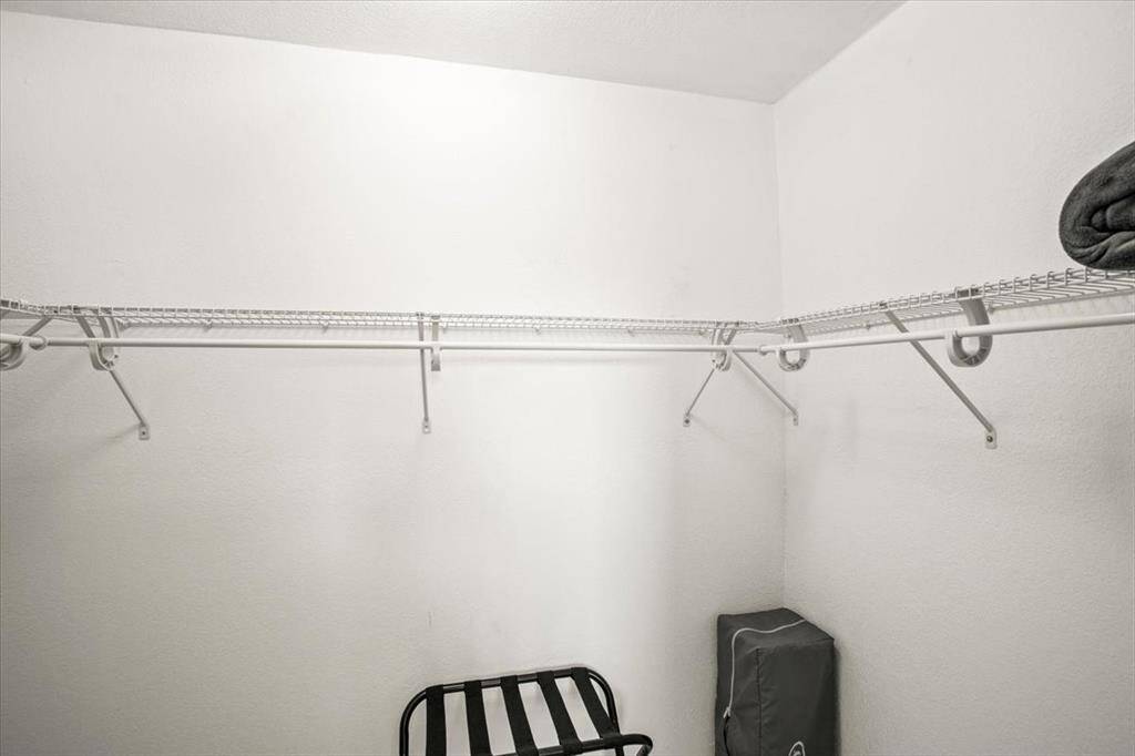 This is a  walk-in closet with built-in metal shelving and rods for hanging clothes, featuring a clean white interior and a single chair for convenience.
