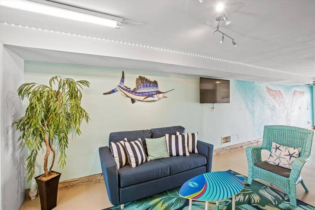 This image shows a cozy, beach-themed living area with artistic wall accents, a comfortable couch, decorative lighting, and a flat-screen TV, perfect for relaxed living or entertaining.