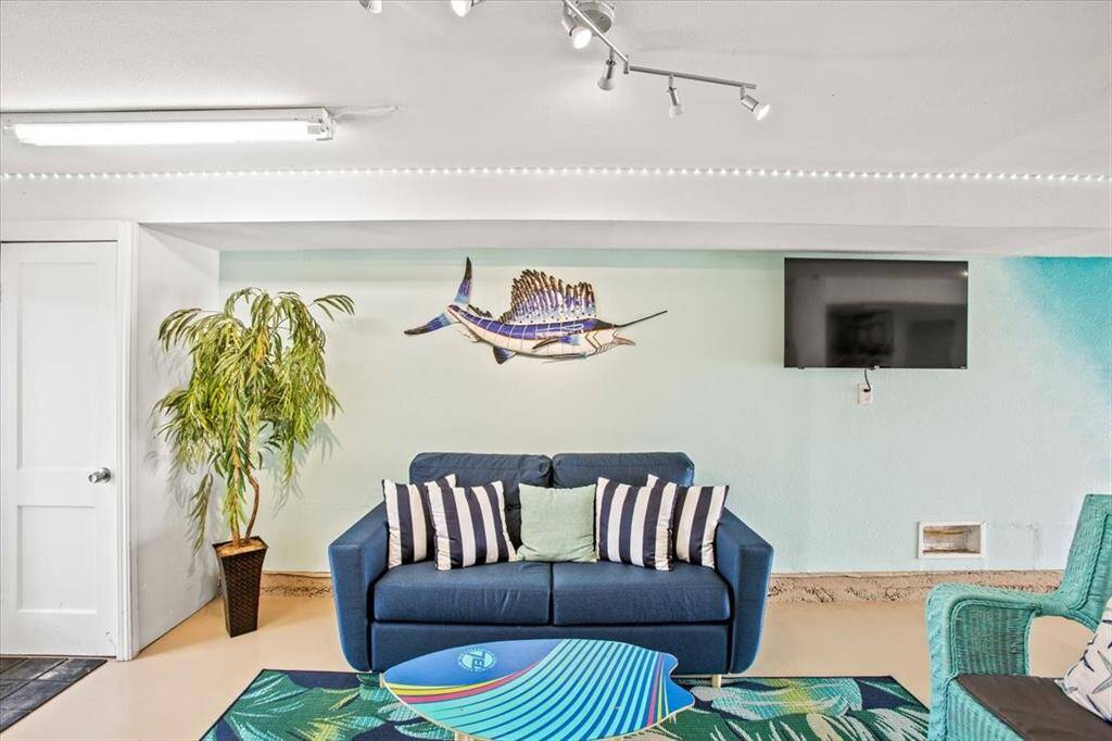 This is a brightly lit, beach-themed living room with a playful color scheme, featuring comfortable seating, track lighting, and a wall-mounted TV.
