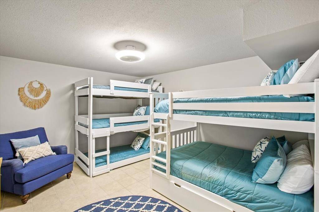 This is a well-maintained, cozy bedroom featuring two sets of white bunk beds with blue bedding, a comfortable blue sofa, and a decorative wall piece. The room has a clean, bright feel, suitable for multiple occupants.
