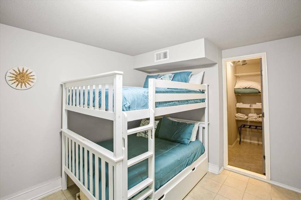 Bunk Room! Featuring a white bunk bed with blue bedding, a small decorative item on the wall, and a closet stocked with linens. The room has tiled flooring and a neutral color palette.