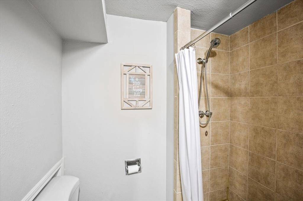 Downstairs bathroom with beige tiled shower walls, a white curtain, and modern fixtures.