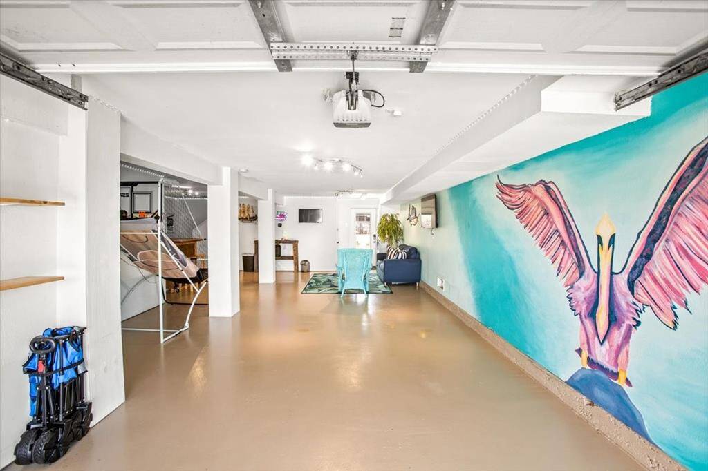 This is a spacious, industrial-style open-plan living area featuring exposed beams and ductwork, with a bold mural for an artistic touch. The space includes a casual seating area and has potential for versatile use.