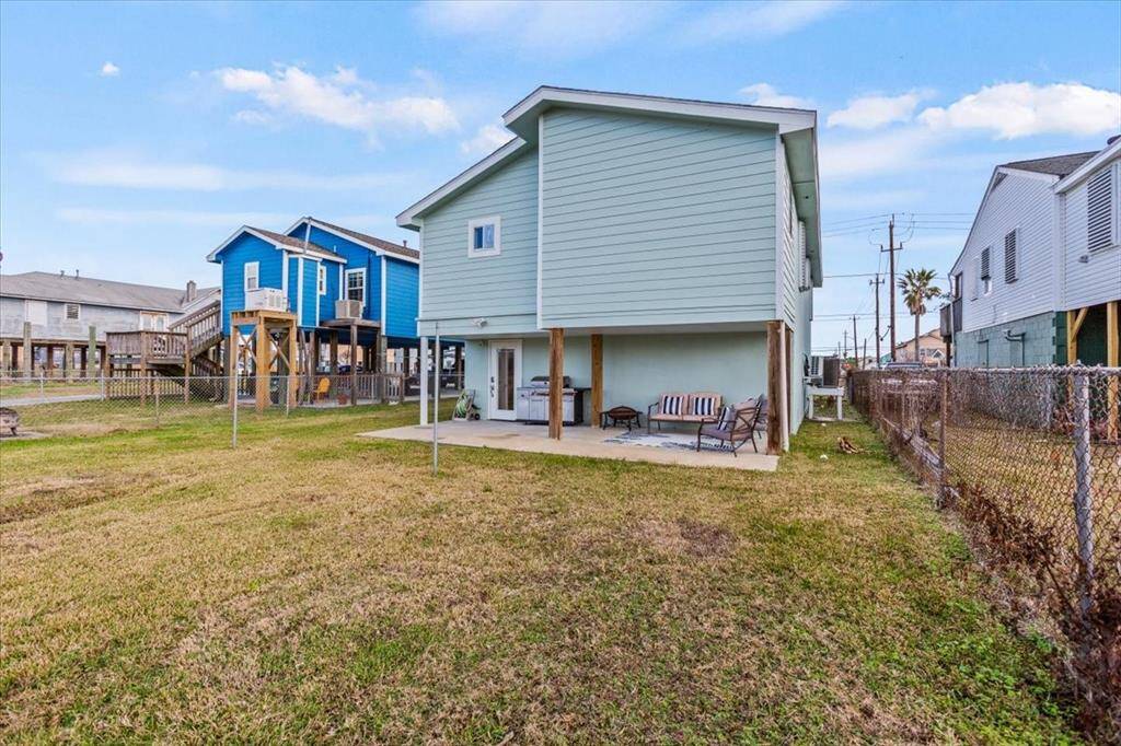 This is a two-story home with a light blue exterior and white trim, featuring a spacious, fenced backyard and a covered patio area on the ground level. The house is part of a neighborhood with similar style homes.