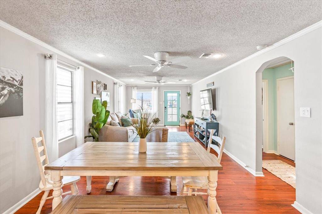 This photo showcases a bright and airy open-plan living space with a combined dining area. It features hardwood floors, ample natural light from multiple windows, and a neutral color palette. The space is well-appointed with modern furnishings and a ceiling fan, providing a comfortable and inviting atmosphere.