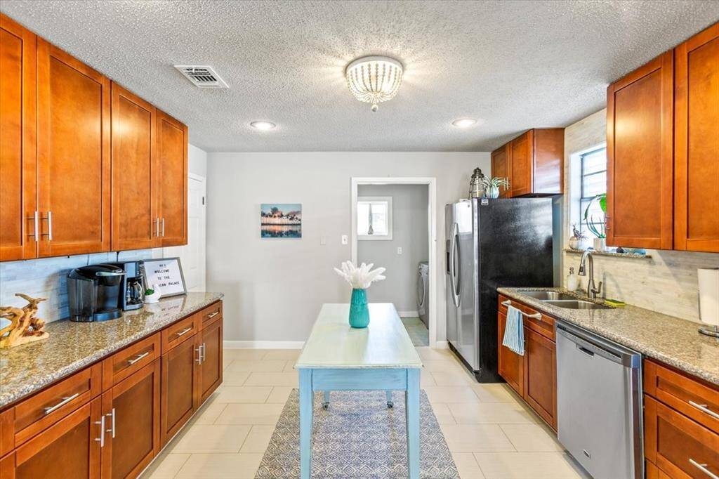 This is a well-lit, modern kitchen with ample cabinet space in a warm wood finish, granite countertops, stainless steel appliances, and a tile floor. A central island adds additional workspace and seating options.