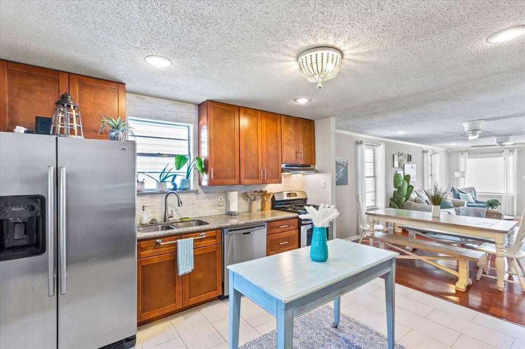 This photo showcases a bright, open-concept kitchen with stainless steel appliances, wooden cabinetry, and a tile backsplash, leading into a cozy dining area with hardwood floors and ample natural light.