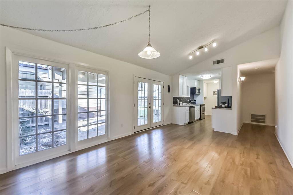 This bright, open-concept space features a living area with hardwood floors and large French doors leading to a patio. The adjacent kitchen is modern, with white cabinetry and stainless steel appliances, offering a seamless flow for entertaining.