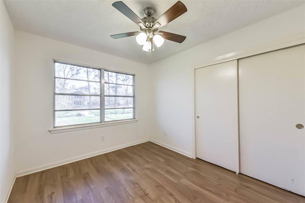 This room features a large window providing ample natural light, closet with sliding doors. The flooring is wood, adding a warm touch to the neutral-toned space.