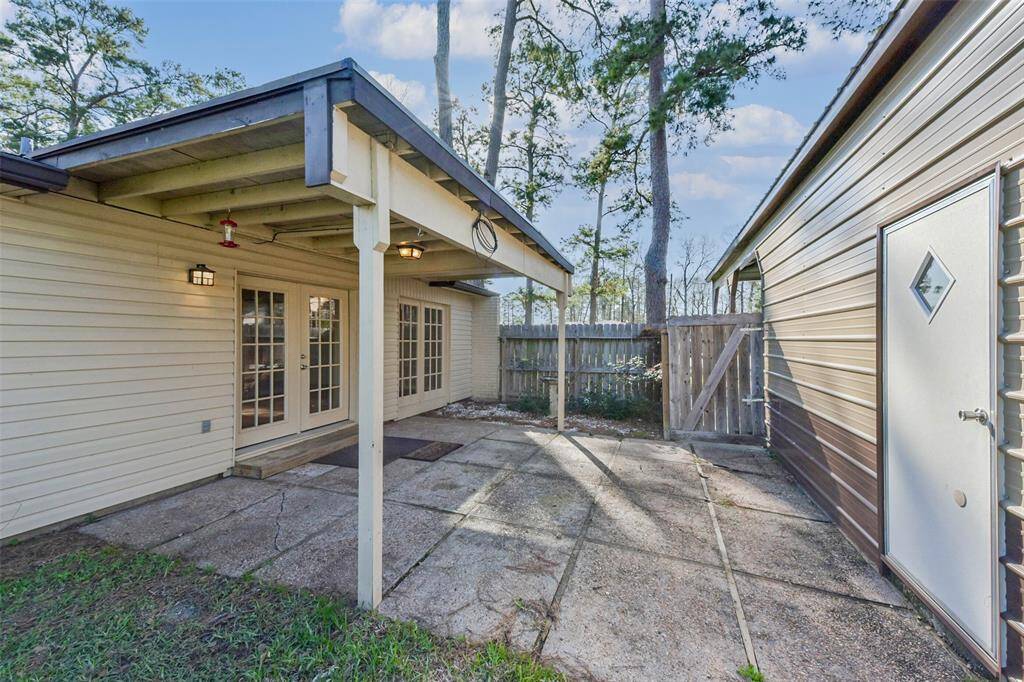 This photo shows a cozy backyard patio area with a covered section, adjacent to a home with French doors. There's a fenced yard and a garage or storage building on the right side, offering privacy and functional outdoor space.