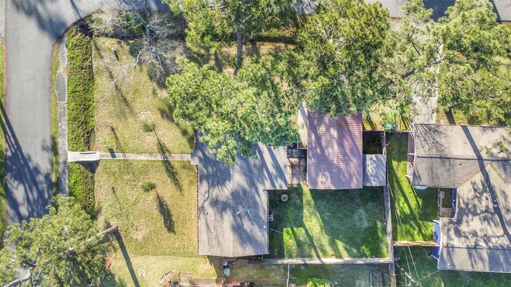 This aerial view shows a property with a house surrounded by mature trees, offering a spacious yard. The home is located on a corner lot, providing additional privacy and space.