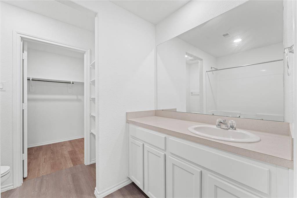 Bathroom with a single vanity, a large mirror, and a bathtub with a shower.