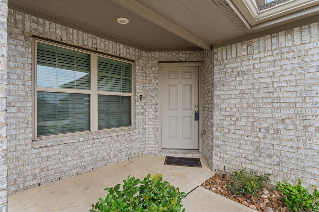 Covered entrance walkway lined with small shrubs and decorative stones, leading to the front door.