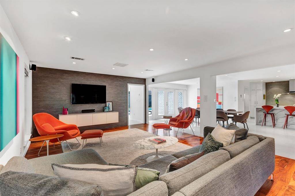 Radiating warmth, this inviting living space is anchored by a floor-to-ceiling accent wall clad in timeless interlocking porcelain tile, adding warmth and sophistication. The wall of glass-front French doors seamlessly connects to your private outdoor oasis, enhancing the home’s effortless indoor-outdoor flow. A doorway leads to the art room, while the open layout extends into the expansive dining room and kitchen, making this home perfectly appointed for both grand entertaining and quiet evenings at home.