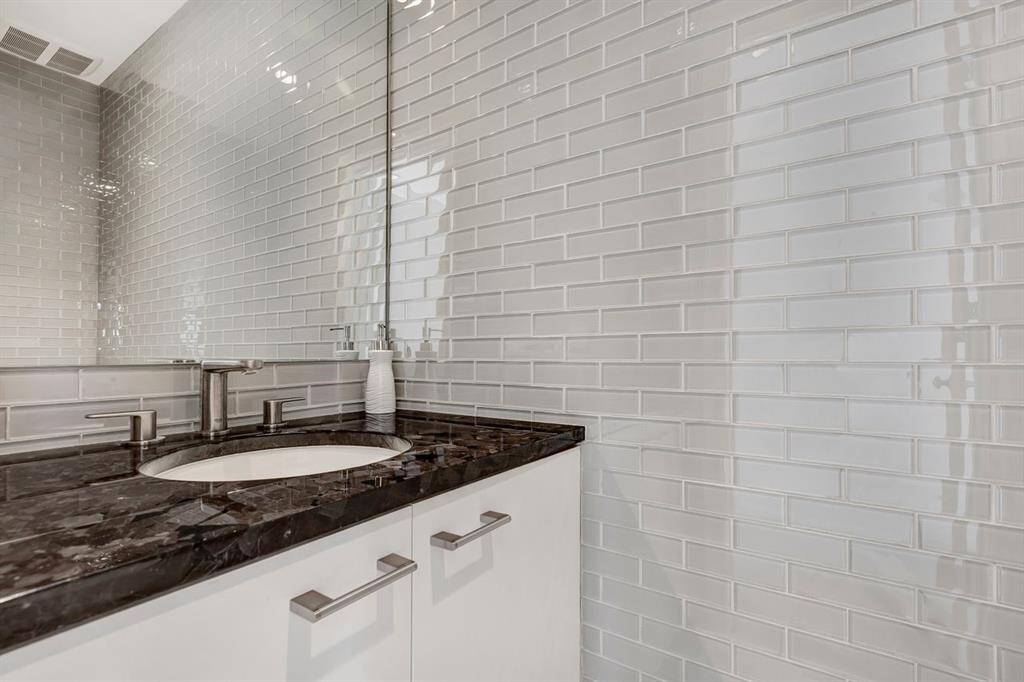 Impeccably designed, this elegantly appointed powder room exudes luxury and refinement, featuring a wall-to-ceiling glass tile surround that enhances depth and sophistication. The rich Antique Brown granite countertop adds a timeless touch, while its convenient location off the foyer ensures both style and functionality for guests.