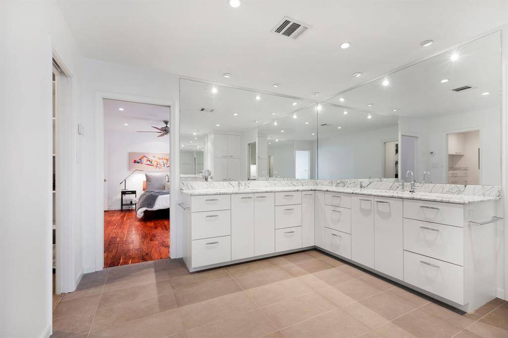 The 2007 second-story renovation introduces a modern dual vanity ensemble featuring Arabescato white marble countertops, custom painted cabinetry, and expansive mirrors. Designed with both style and functionality in mind, the space also includes a private toilet room with additional storage and commercial-rated porcelain tile flooring for durability and timeless appeal.