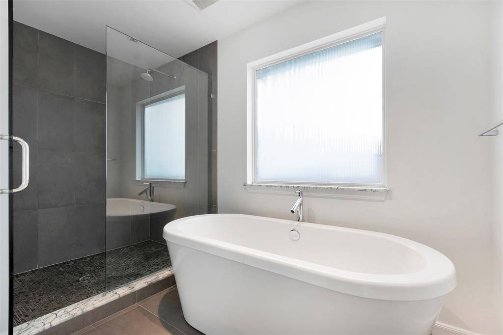 Designed for tranquility, the private bath area features a freestanding tub paired with high-design commercial-grade plumbing fixtures, creating a spa-like retreat. An oversized walk-in shower, fully tiled and enclosed by a glass partition, enhances the modern aesthetic, while commercial-rated porcelain flooring ensures lasting durability and style.