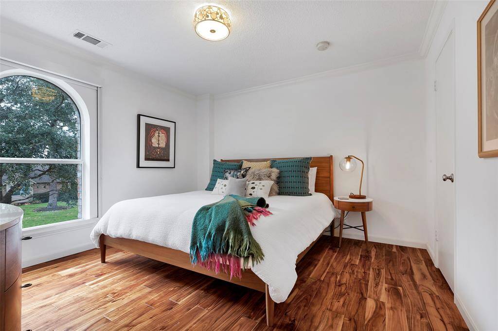 A streamlined upstairs secondary bedroom at the front of the home showcases warm acacia wood flooring, a spacious walk-in closet, and a minimalist modern aesthetic. Large arched windows invite abundant natural light, enhancing the bright and uncluttered design.
