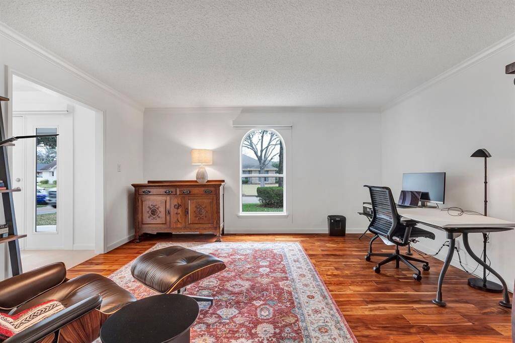 Revealing another angle of the office, this photo highlights its spacious layout and architectural details. To the left, the foyer provides a seamless entry into the home, while crown molding adds a refined touch to the space.