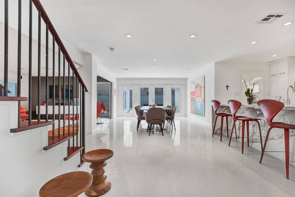 Upon entering, the home immediately impresses with its expansive sightlines and seamless flow. A stunning wall of French doors at the far end bathes the space in natural light, drawing the eye toward the private outdoor retreat. The polished porcelain tile flooring, rich wood accents, and statement marble island set the tone for a home defined by modern luxury and refined elegance.